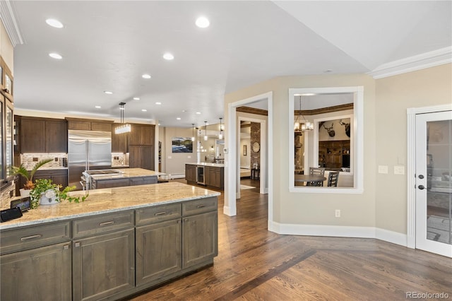 kitchen with built in fridge, lofted ceiling, decorative light fixtures, light stone counters, and crown molding