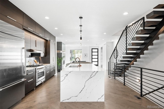 kitchen with sink, hanging light fixtures, an island with sink, premium appliances, and wood-type flooring