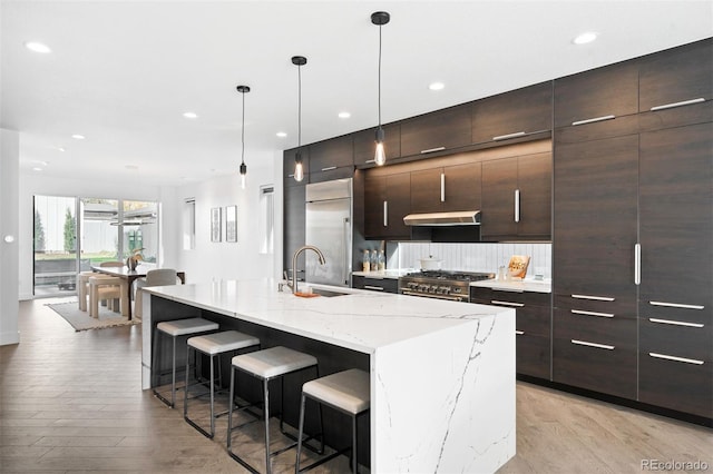 kitchen with a breakfast bar, high end appliances, a kitchen island with sink, sink, and light wood-type flooring