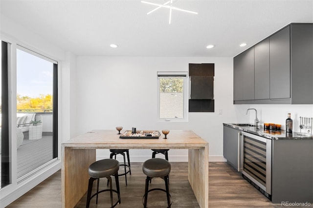 kitchen featuring gray cabinetry, sink, beverage cooler, a breakfast bar area, and hardwood / wood-style flooring