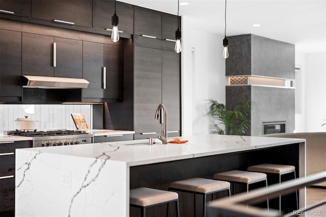 kitchen featuring a kitchen breakfast bar, sink, decorative backsplash, decorative light fixtures, and light stone counters