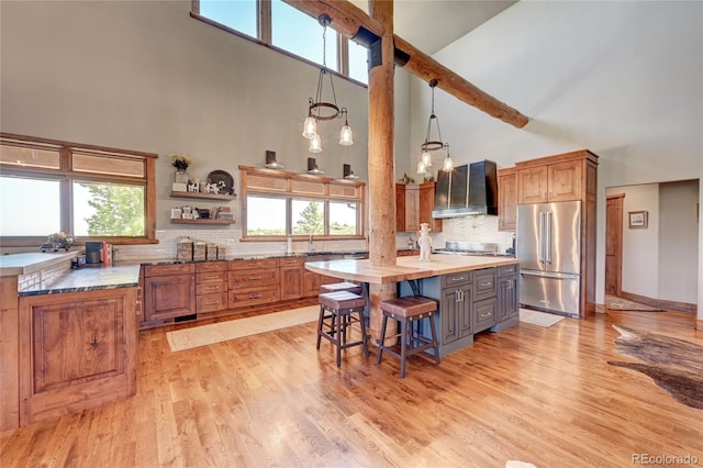 kitchen with a kitchen island, appliances with stainless steel finishes, high vaulted ceiling, wall chimney range hood, and beam ceiling