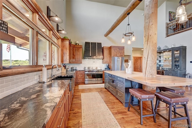 kitchen with a towering ceiling, a kitchen bar, decorative backsplash, stainless steel appliances, and wall chimney range hood