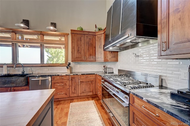 kitchen with sink, tasteful backsplash, light wood-type flooring, stainless steel appliances, and wall chimney range hood