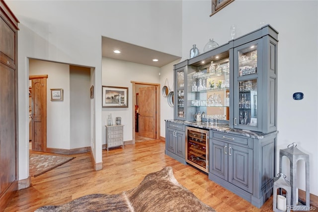 bar with beverage cooler, stone counters, and light wood-type flooring