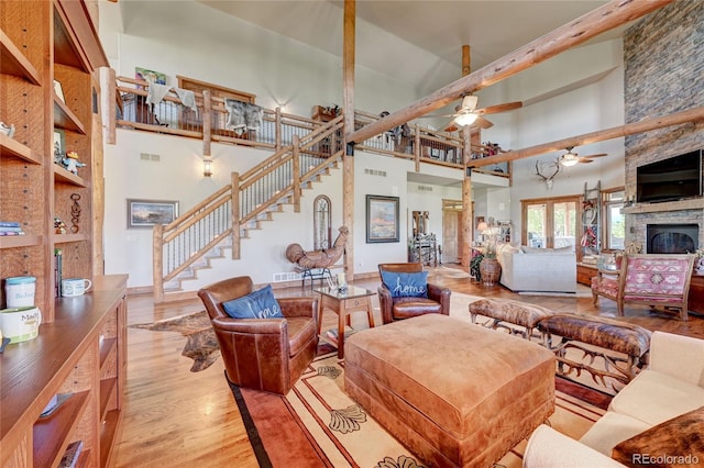 living room featuring ceiling fan, a towering ceiling, a fireplace, and light hardwood / wood-style flooring