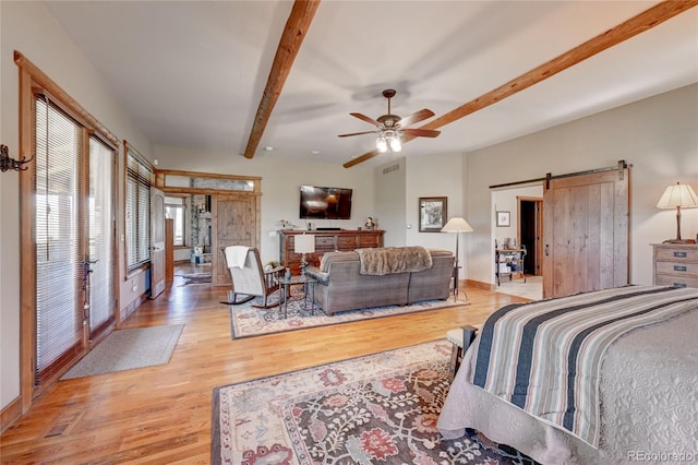 bedroom with ceiling fan, a barn door, light hardwood / wood-style floors, and beam ceiling