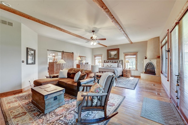 living room with ceiling fan, beam ceiling, light hardwood / wood-style floors, a large fireplace, and a barn door