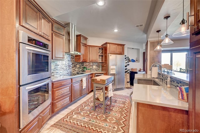 kitchen with pendant lighting, sink, wall chimney range hood, stainless steel appliances, and decorative backsplash