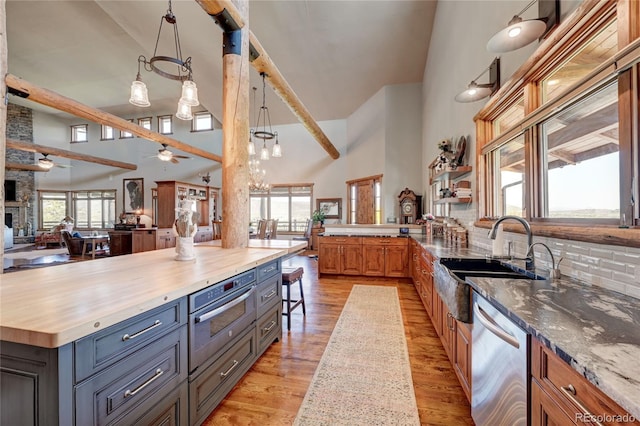 kitchen featuring sink, butcher block countertops, decorative light fixtures, high vaulted ceiling, and dishwasher