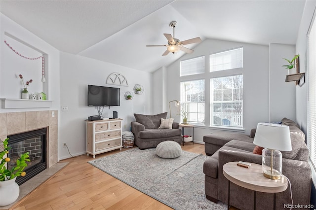 living room with vaulted ceiling, ceiling fan, a fireplace, and light hardwood / wood-style flooring