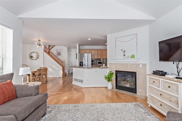 living room featuring an inviting chandelier, a tile fireplace, vaulted ceiling, and light hardwood / wood-style flooring