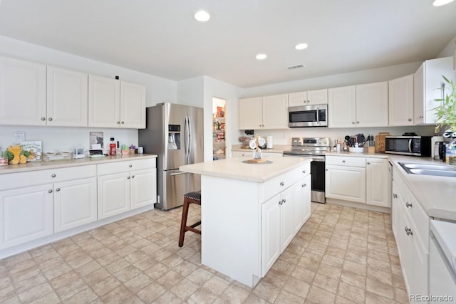 kitchen featuring appliances with stainless steel finishes, a kitchen breakfast bar, sink, a center island, and white cabinetry