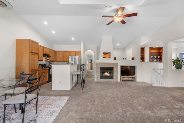 kitchen featuring black gas range, stainless steel refrigerator with ice dispenser, lofted ceiling, a kitchen breakfast bar, and light colored carpet