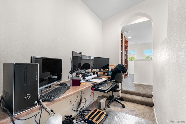 carpeted home office with arched walkways, a textured wall, and lofted ceiling