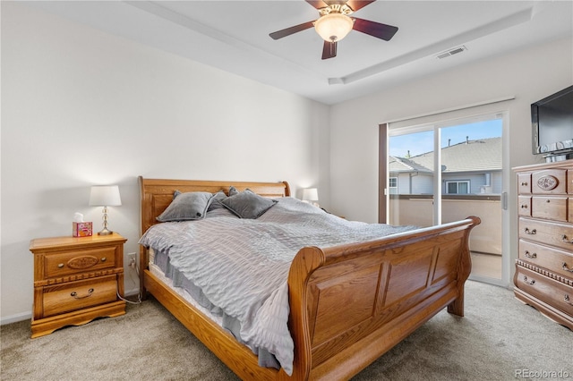 bedroom with light colored carpet, a tray ceiling, and a ceiling fan