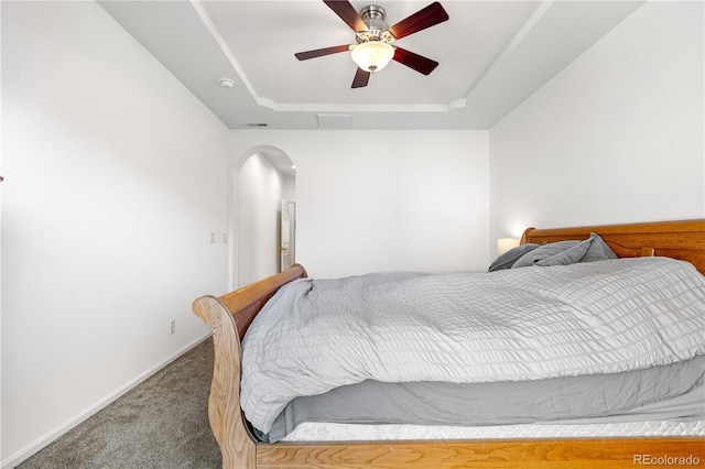 carpeted bedroom featuring arched walkways, a raised ceiling, a ceiling fan, and baseboards