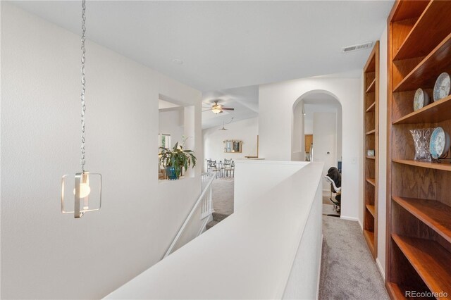hallway featuring carpet floors, arched walkways, built in shelves, and an upstairs landing