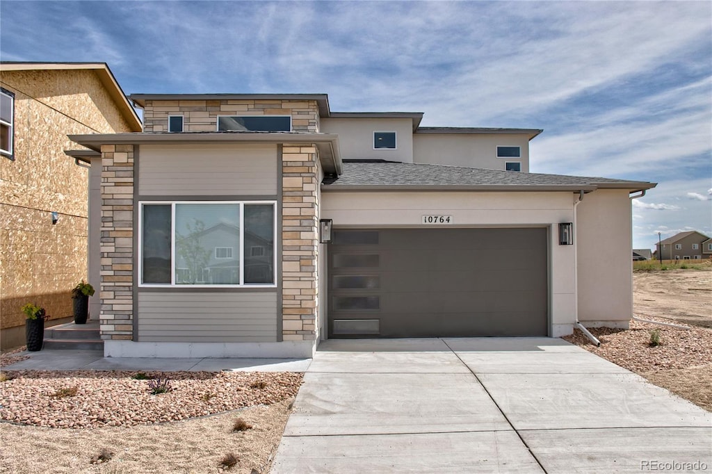 view of front of home featuring concrete driveway, an attached garage, stone siding, and stucco siding