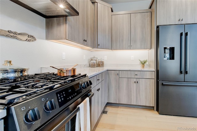 kitchen featuring wall chimney range hood, light brown cabinetry, light hardwood / wood-style floors, and stainless steel appliances