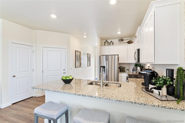 22323 E 6th Pl, Aurora, CO 80018 - kitchen featuring wood finished floors, stainless steel appliances, a peninsula, white cabinetry, and light stone countertops
