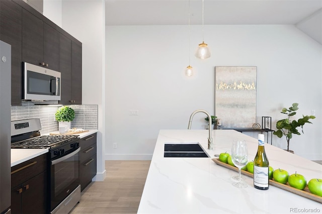 kitchen featuring pendant lighting, decorative backsplash, light wood-type flooring, light stone countertops, and stainless steel appliances