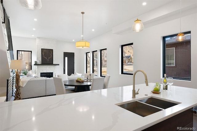 kitchen featuring a fireplace, light stone counters, sink, and pendant lighting