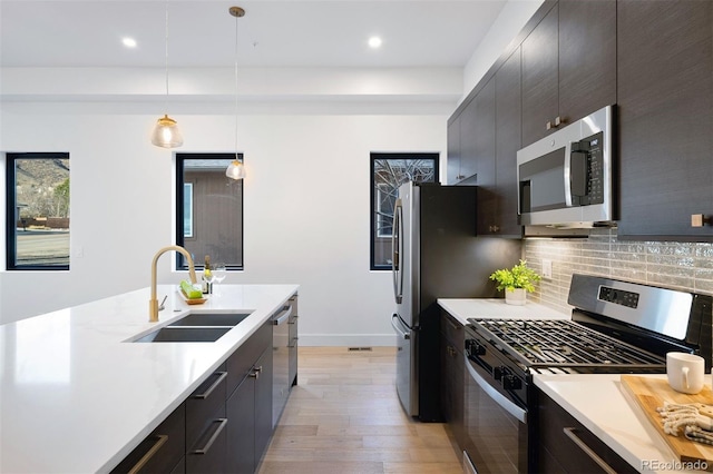 kitchen with backsplash, decorative light fixtures, stainless steel appliances, light countertops, and a sink