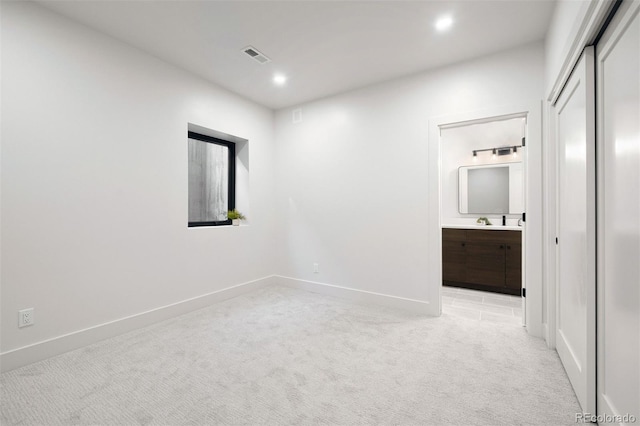 empty room with recessed lighting, light colored carpet, a sink, visible vents, and baseboards