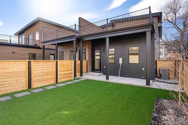 back of house featuring central air condition unit, a balcony, a fenced backyard, and a lawn