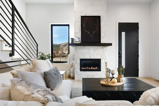 living room featuring light wood finished floors, stairway, a tile fireplace, and baseboards