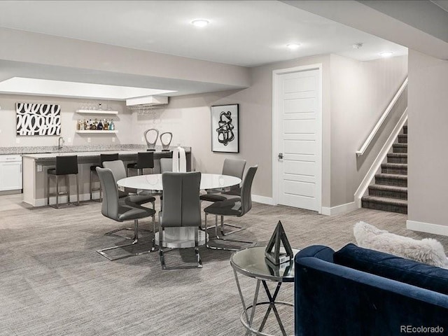 dining space featuring light colored carpet, wet bar, baseboards, and stairway