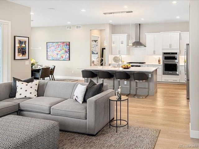 living room featuring light wood-style flooring, baseboards, visible vents, and recessed lighting