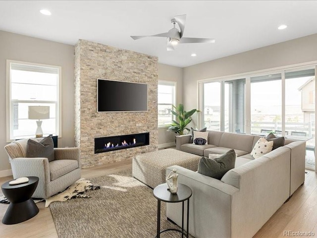 living area with a stone fireplace, light wood-style flooring, a ceiling fan, and recessed lighting