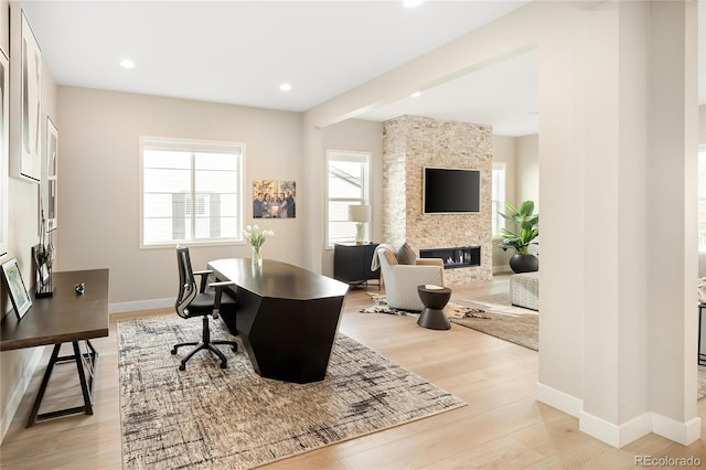 office space featuring baseboards, light wood-type flooring, recessed lighting, and a fireplace
