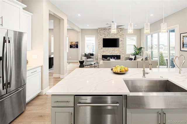 kitchen with light stone counters, open floor plan, light wood-style flooring, stainless steel appliances, and a sink
