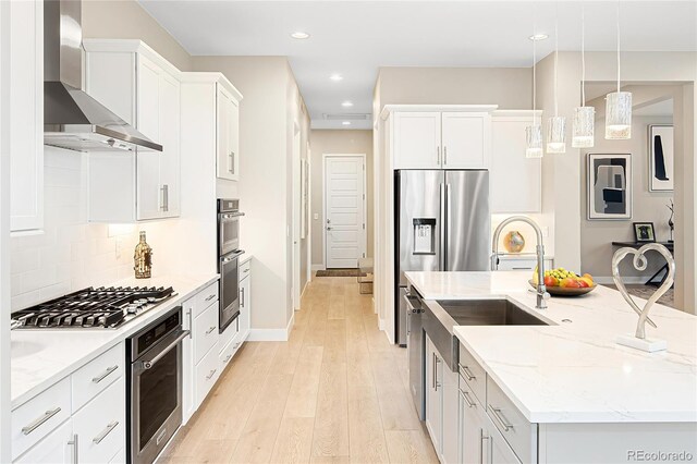 6530 Barnstead Dr, Castle Pines, CO 80108 - kitchen with wall chimney exhaust hood, appliances with stainless steel finishes, an island with sink, light wood-style flooring, and light stone countertops
