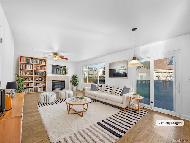 living room with a tiled fireplace, a ceiling fan, and wood finished floors