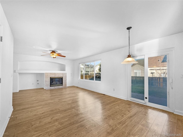 unfurnished living room with a tiled fireplace, baseboards, a ceiling fan, and wood finished floors