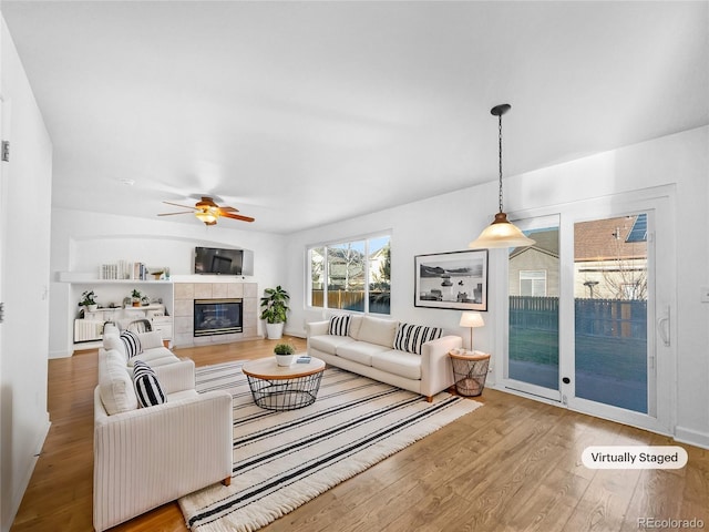 living area featuring ceiling fan, wood finished floors, and a tiled fireplace