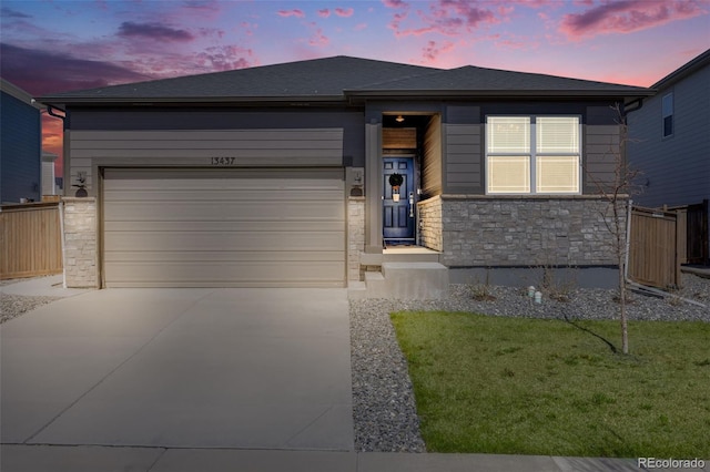 view of front of property with fence, stone siding, concrete driveway, an attached garage, and a yard