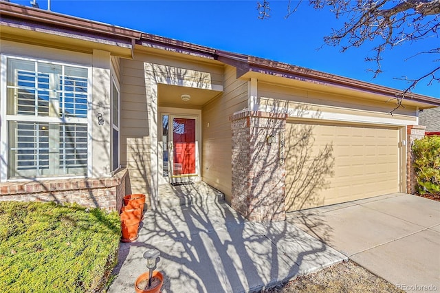 doorway to property with a garage, brick siding, and driveway