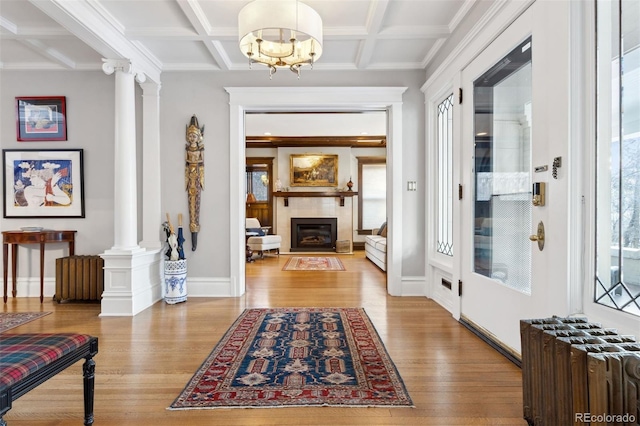 foyer entrance featuring coffered ceiling, radiator heating unit, decorative columns, and light hardwood / wood-style floors