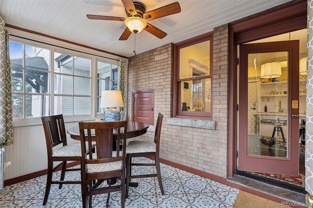 dining room with ceiling fan, ornamental molding, and brick wall