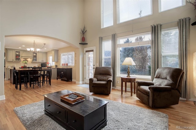 living room with an inviting chandelier, arched walkways, light wood-style floors, and a towering ceiling