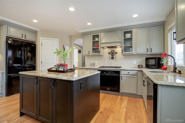 kitchen featuring a sink, arched walkways, custom range hood, a kitchen island, and black appliances