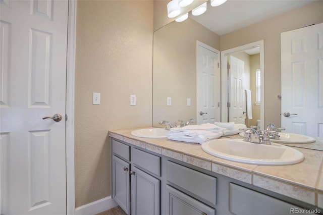 full bathroom featuring a sink, a textured wall, and double vanity