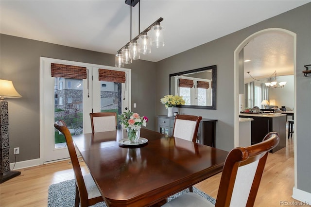 dining area with arched walkways, a notable chandelier, plenty of natural light, and light wood finished floors