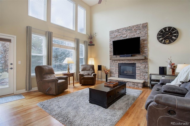 living room with a fireplace, light wood-type flooring, plenty of natural light, and a towering ceiling