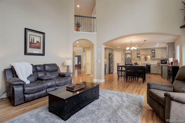 living area featuring a high ceiling, a notable chandelier, arched walkways, recessed lighting, and light wood-type flooring